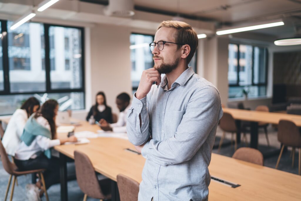 Thoughtful,Young,Businessman,Standing,In,Modern,Coworking,Office,,Looking,Away